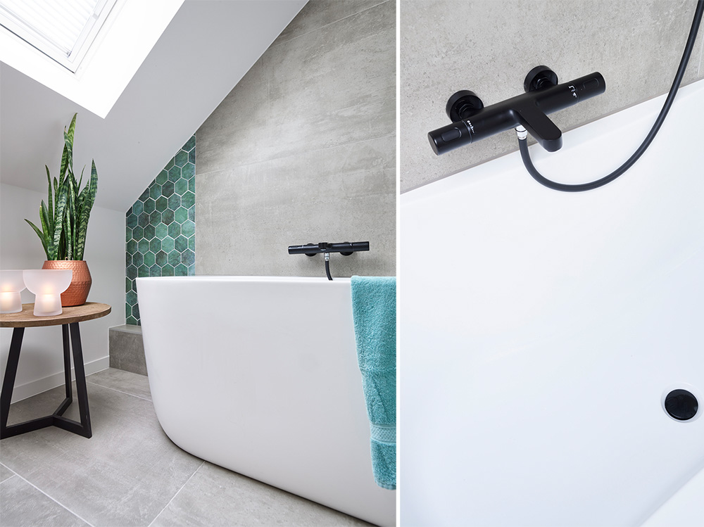 Badkamer met een modern ligbad, zwarte kraan, groene tegels en een plant op een houten tafel.