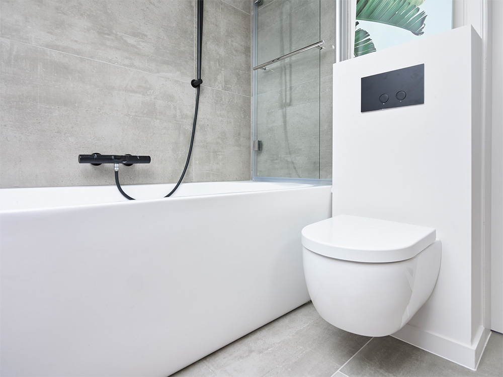 Wit ligbad, zwarte kraan, doucheruimte met glazen wand en een zwevend toilet.