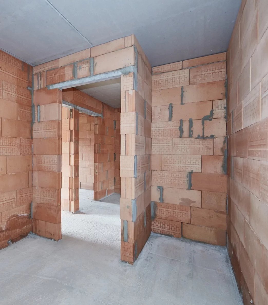 Espace en construction avec des murs en briques et des ouvertures pour les portes et fenêtres.
