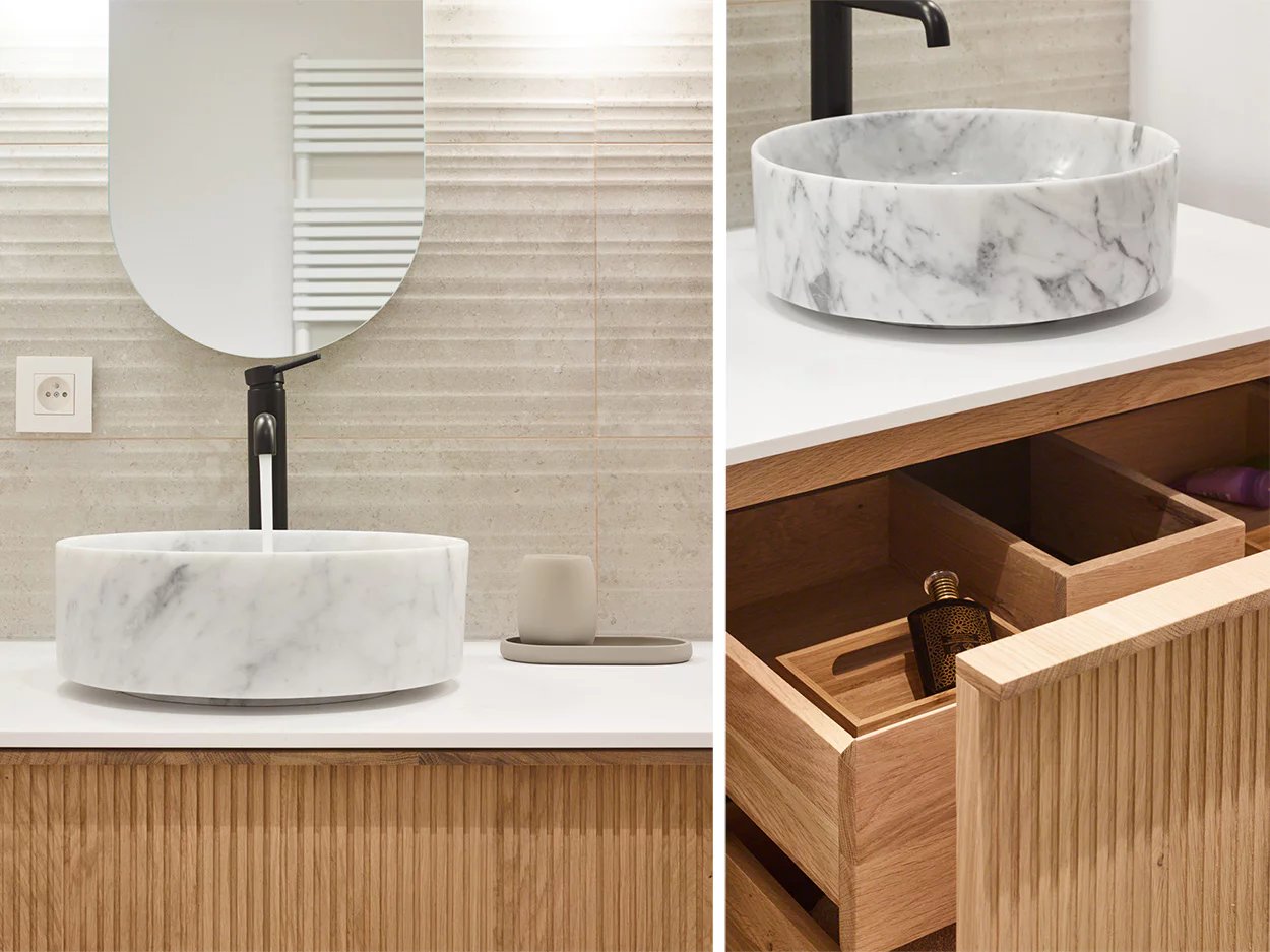 Lavabo en marbre blanc avec robinet noir sur un meuble vasque en bois, avec tiroir ouvert.