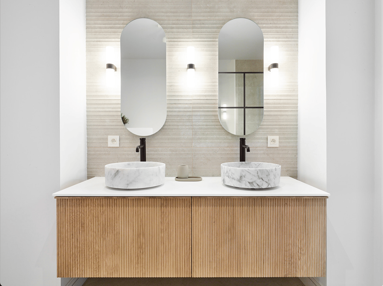 Double lavabo en marbre avec robinets chromés noirs, éclairage élégant et meuble en lin.