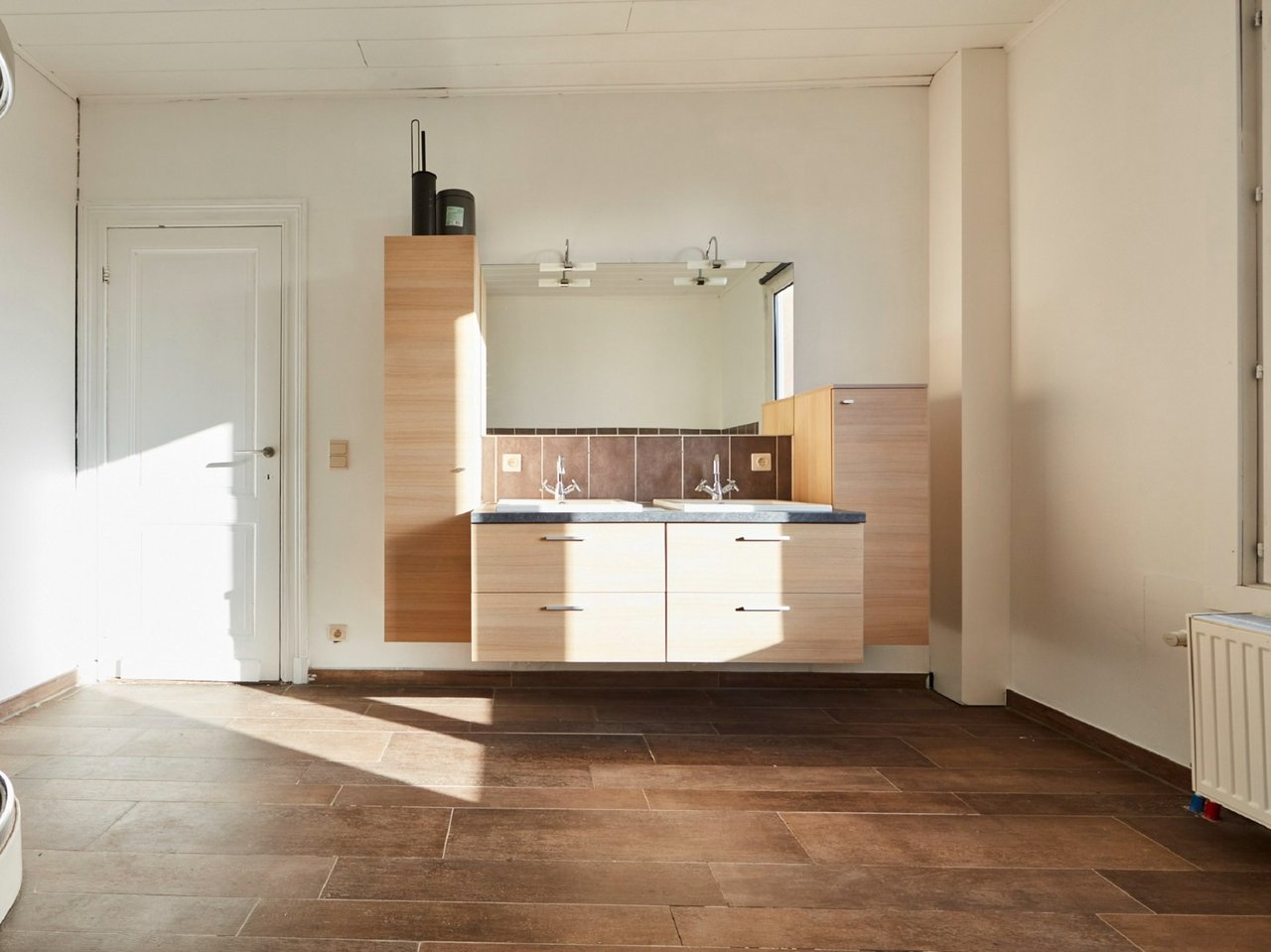 Salle de bain lumineuse avec double lavabo, armoires en bois et un grand miroir au-dessus du plan de travail.