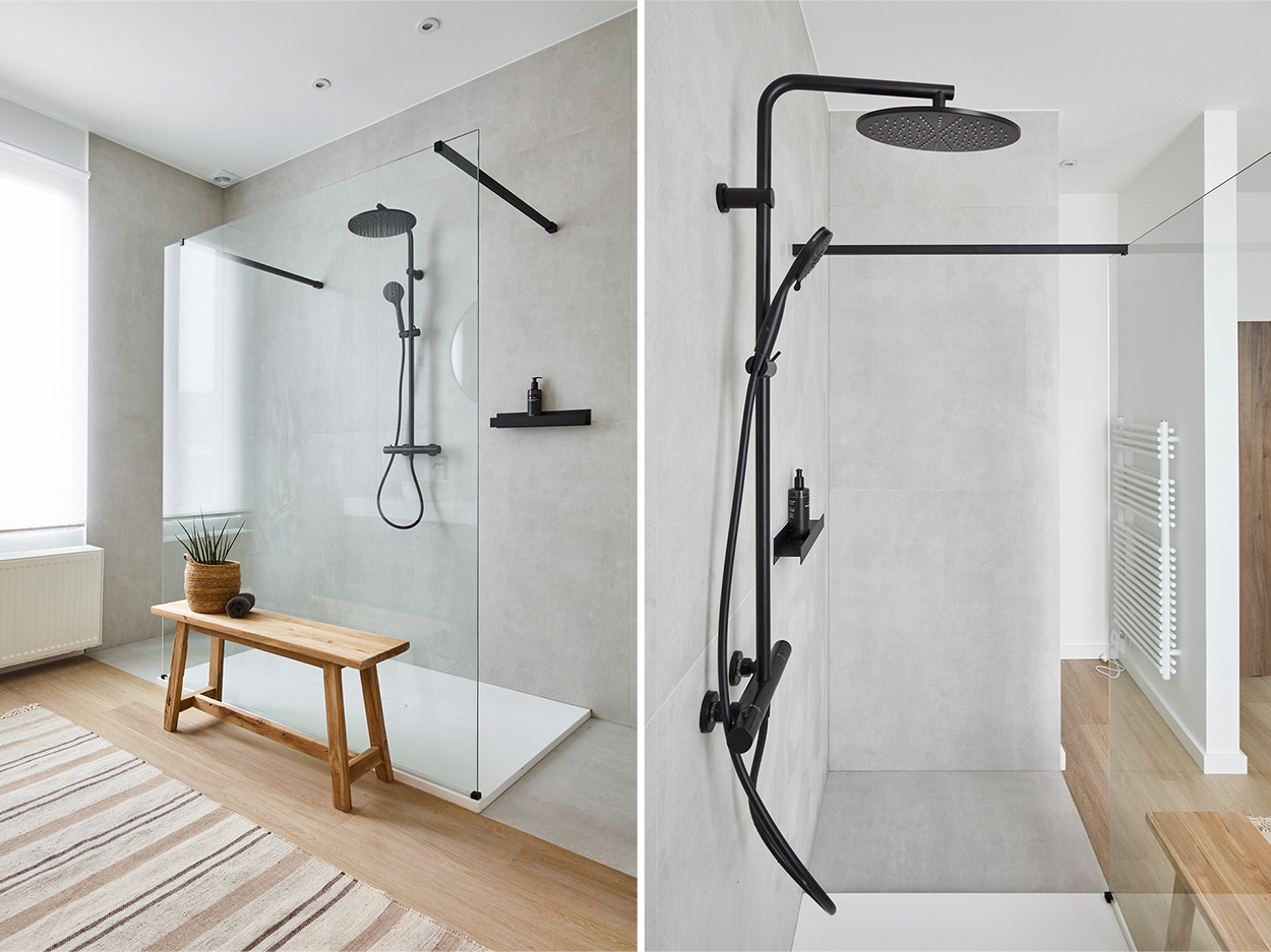 Cabine de douche moderne avec pommeau de douche noir et douchette, un banc en bois et un pot de plantes.