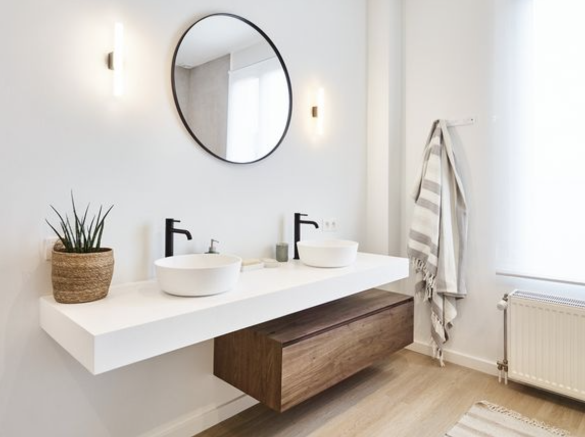 Salle de bain épurée avec deux miroirs ronds, des lavabos et des robinets noirs, accompagnés d'un tiroir en bois.