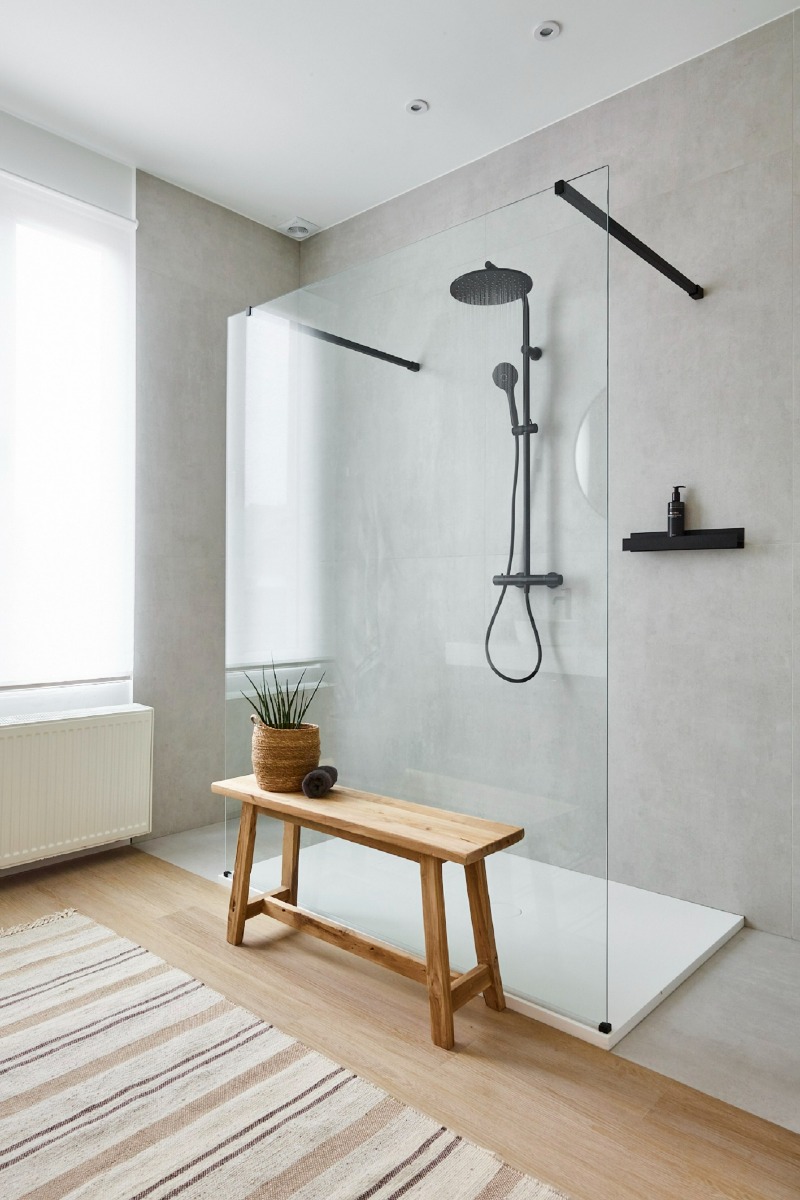 Douche à l'italienne moderne avec une douche à effet pluie noire, paroi en verre et banc en bois.