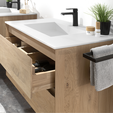 Un meuble de salle de bain avec un lavabo blanc, des tiroirs en bois et un porte-serviette.