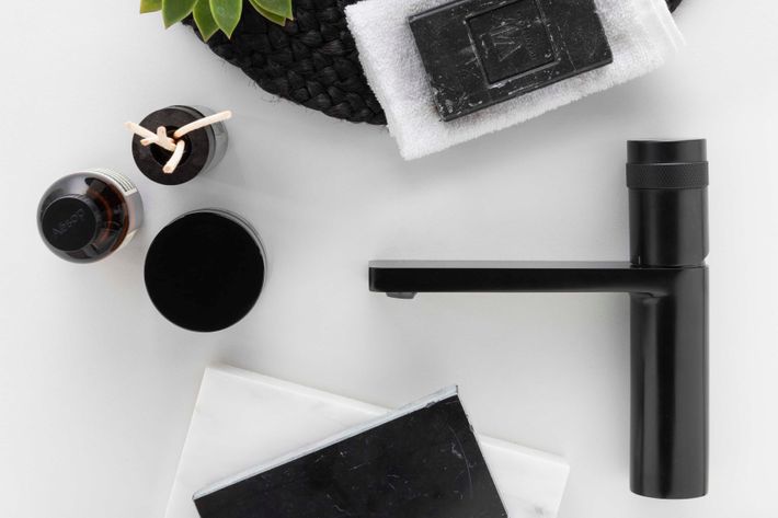 Zwarte wastafelmengkraan, geurverspreider, zeep en handdoek op een wit blad.
