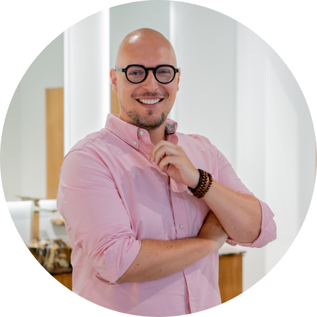 Man met een roze overhemd, bril, en een glimlach, staand in een badkameromgeving.