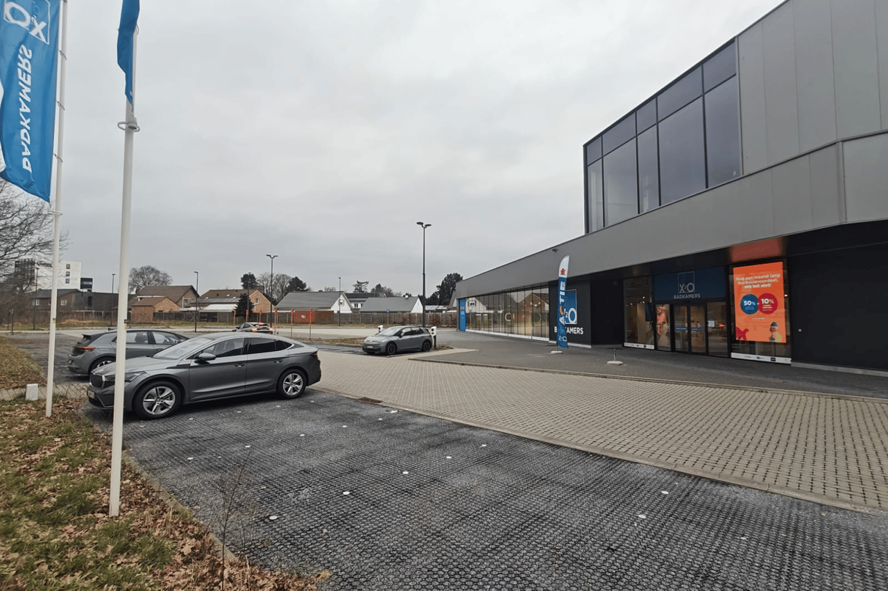 Moderne XO Badkamers-winkel met een deels lege parkeerplaats op een grijze, bewolkte dag in een rustige woonwijk.