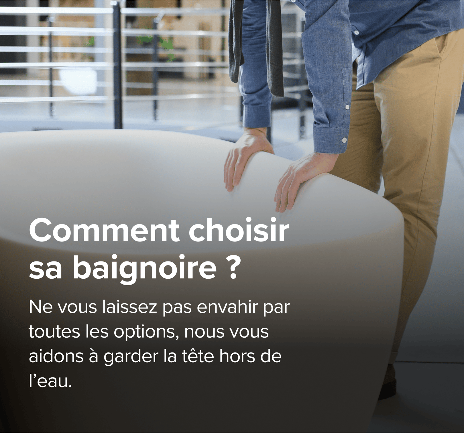 Sur cette image de x²o badkamers, un homme en pantalon beige et chemise bleue examine une grande baignoire design van x²o badkamers in een showroom met een industriële vloer en andere badmodellen op de achtergrond.