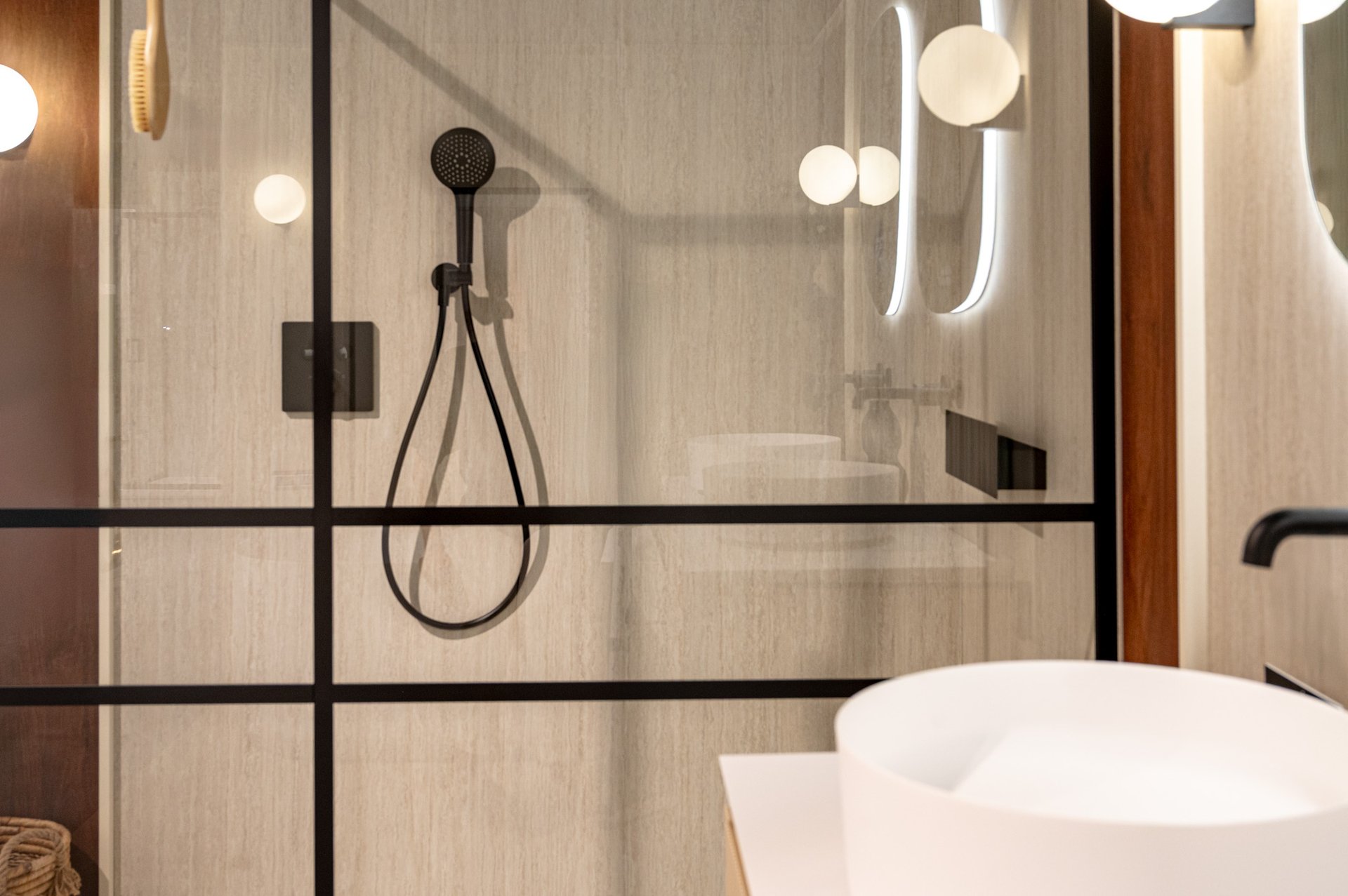 Overzichtsfoto van een complete badkamer van x²o badkamers met een vrijstaand wit ligbad, een zwart wandgemonteerd kraansysteem en een decoratieve kunstprint boven het bad. De combinatie van lichte muren en warme houten accenten zorgt voor een serene en stijlvolle sfeer.