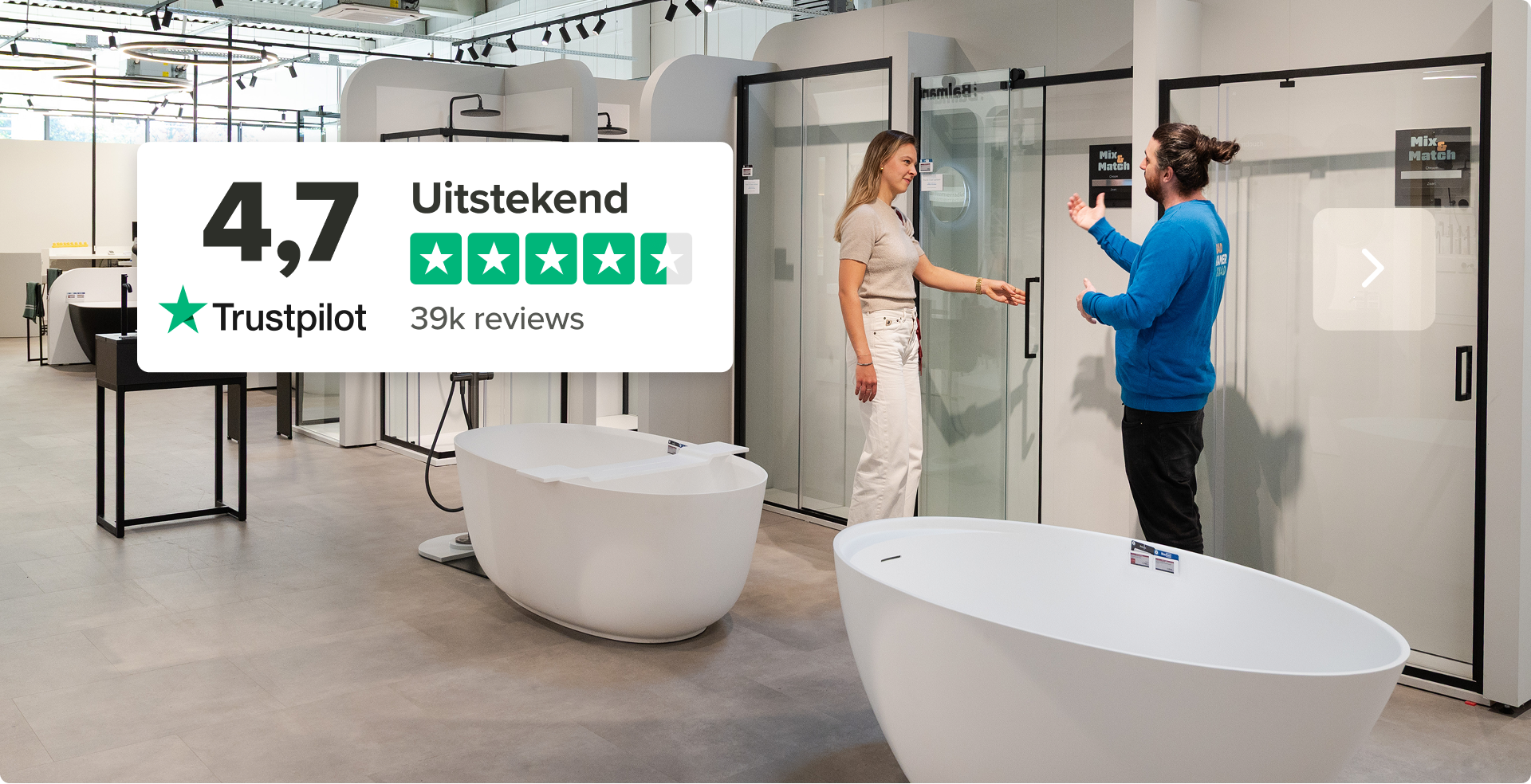 Afbeelding van een ruime showroom van x²o badkamers met moderne vrijstaande baden en glazen douchewanden. Links staat een Trustpilot-score met de tekst “4,7 – Uitstekend”, vijf groene sterren en “39k reviews”. Twee medewerkers zijn in gesprek bij een doucheopstelling, wat de service en expertise van x²o badkamers benadrukt.