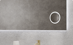 Detailopname van een badkamerspiegel van x²o badkamers met subtiele geïntegreerde LED-verlichting achter de spiegel. Rechts in het spiegeloppervlak is een ronde bedieningsknop zichtbaar tegen een grijze structuurwand.