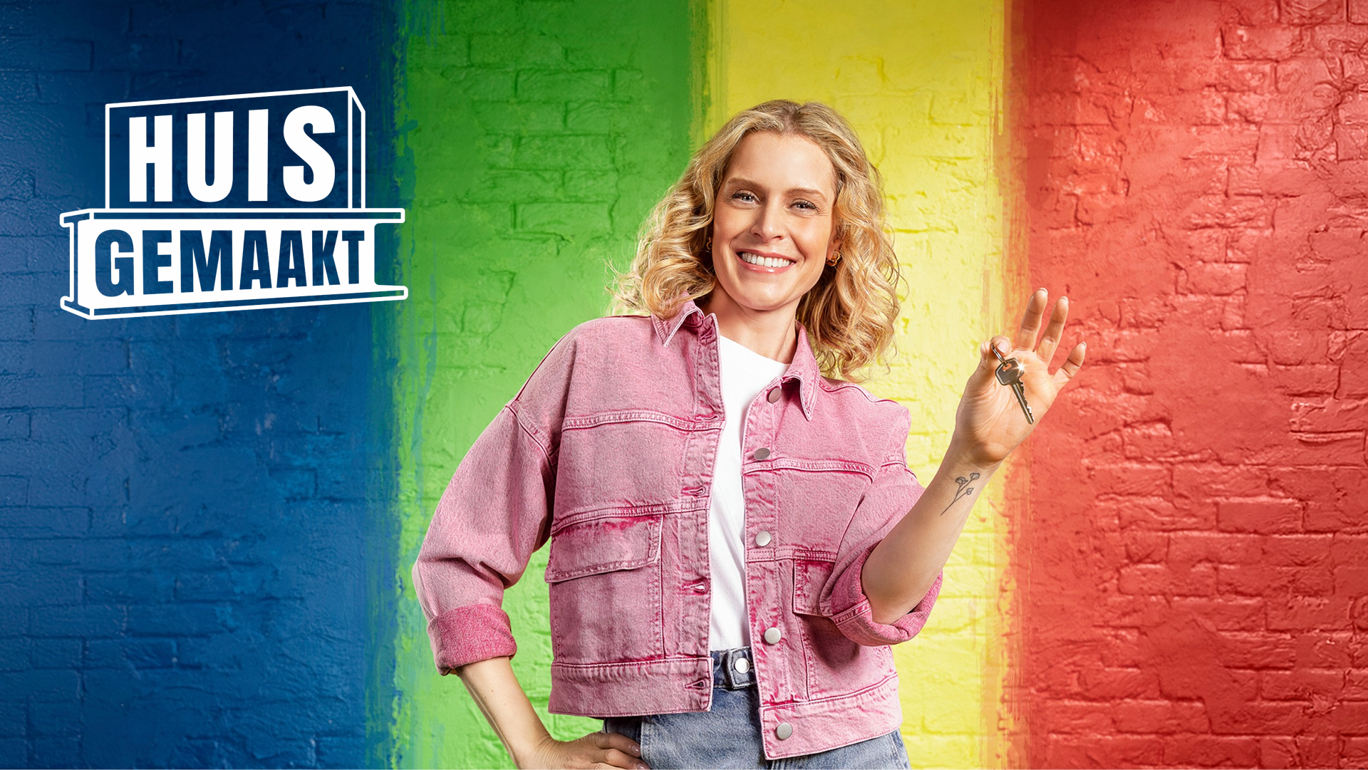 Vrouw met krullend blond haar in roze jeansjasje houdt sleutels omhoog en glimlacht voor een bakstenen muur in regenboogkleuren met de tekst “Huis Gemaakt” en “X²O in Huis Gemaakt”, campagnebeeld van x²o badkamers.