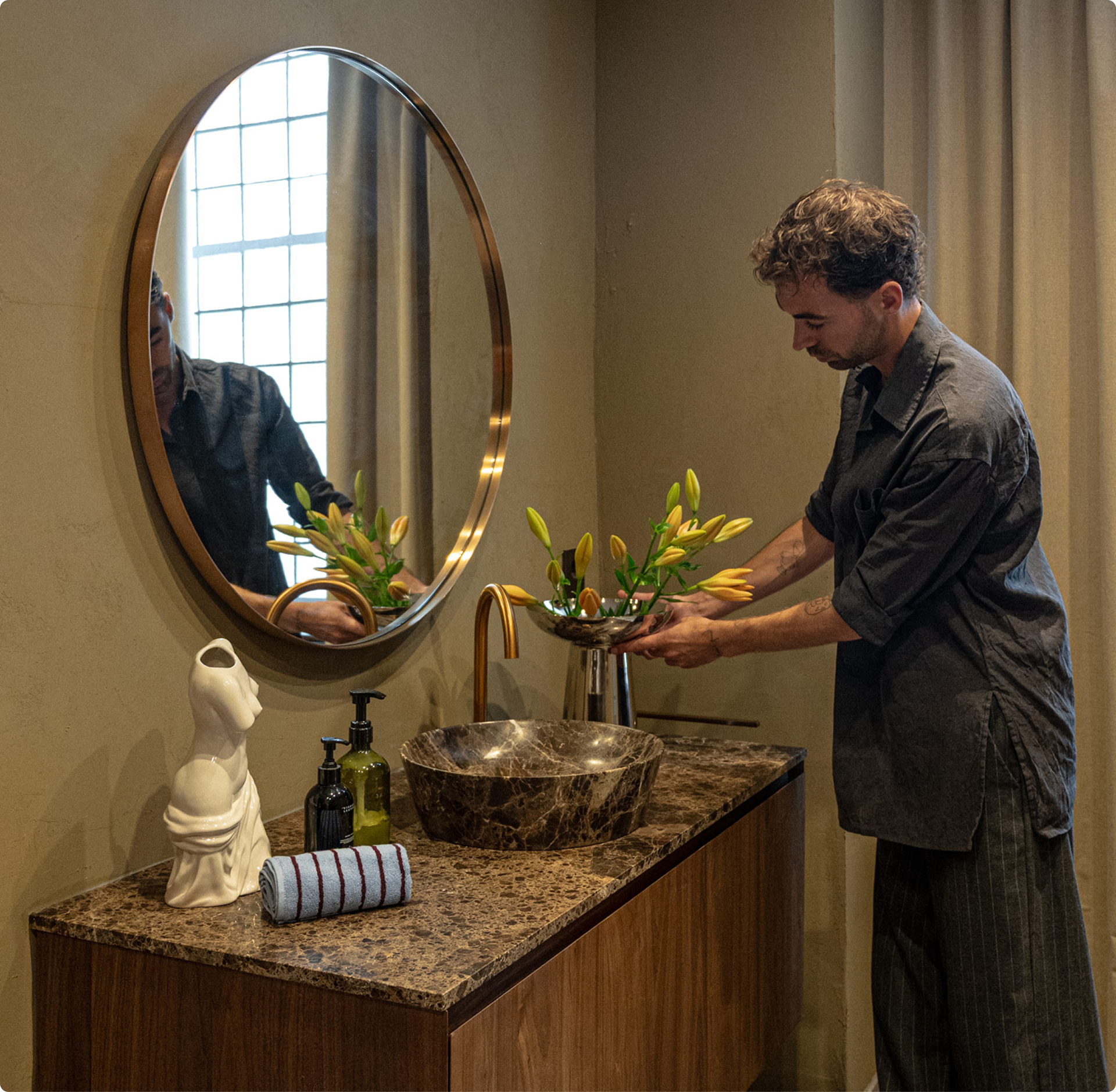 Daan Alferink schikt bloemen aan zijn marmeren wastafel met gouden kraan.