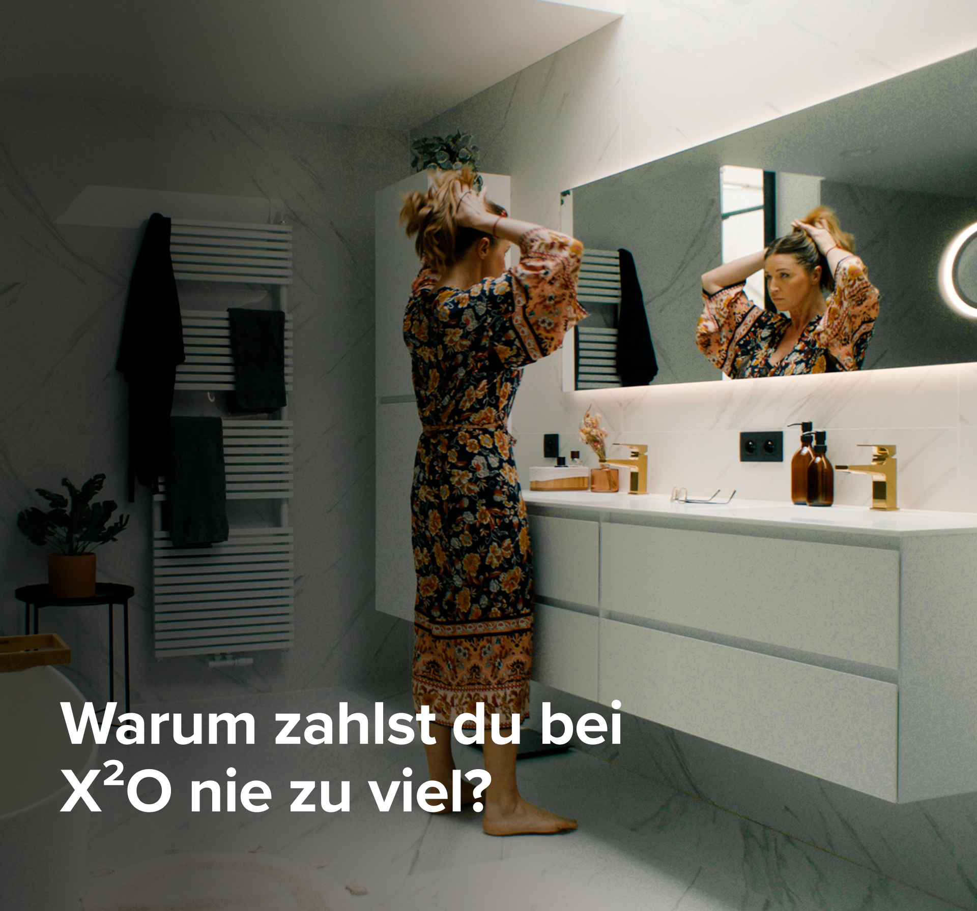 Frau vor dem Spiegel in einem stilvollen Badezimmer mit weißen Marmorwänden, X²O Badezimmer.