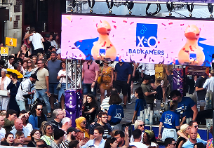 Druk festivalpubliek voor een podium met groot scherm X²O badkamers tijdens het Moenfeest.