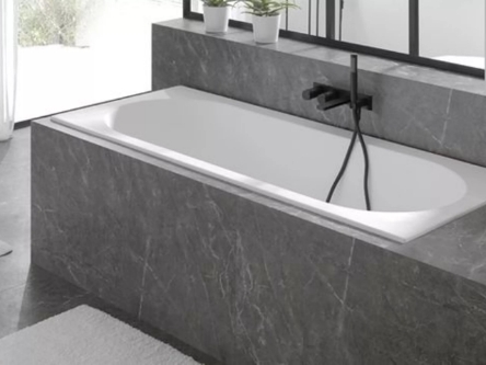 Badkuip ingebouwd in marmeren wand met zwart kraanwerk.