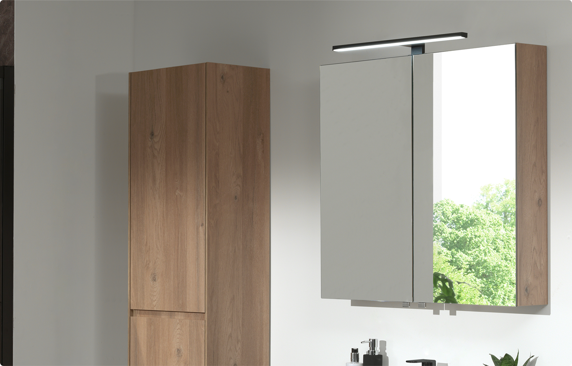 Storke Reflecta Spiegelschrank mit zwei Spiegeltüren und integrierter Oberbeleuchtung, kombiniert mit einem Hochschrank in Roh-Eiche an einer weißen Wand mit einfallendem Tageslicht in einem Badezimmer von x²o Badezimmer.