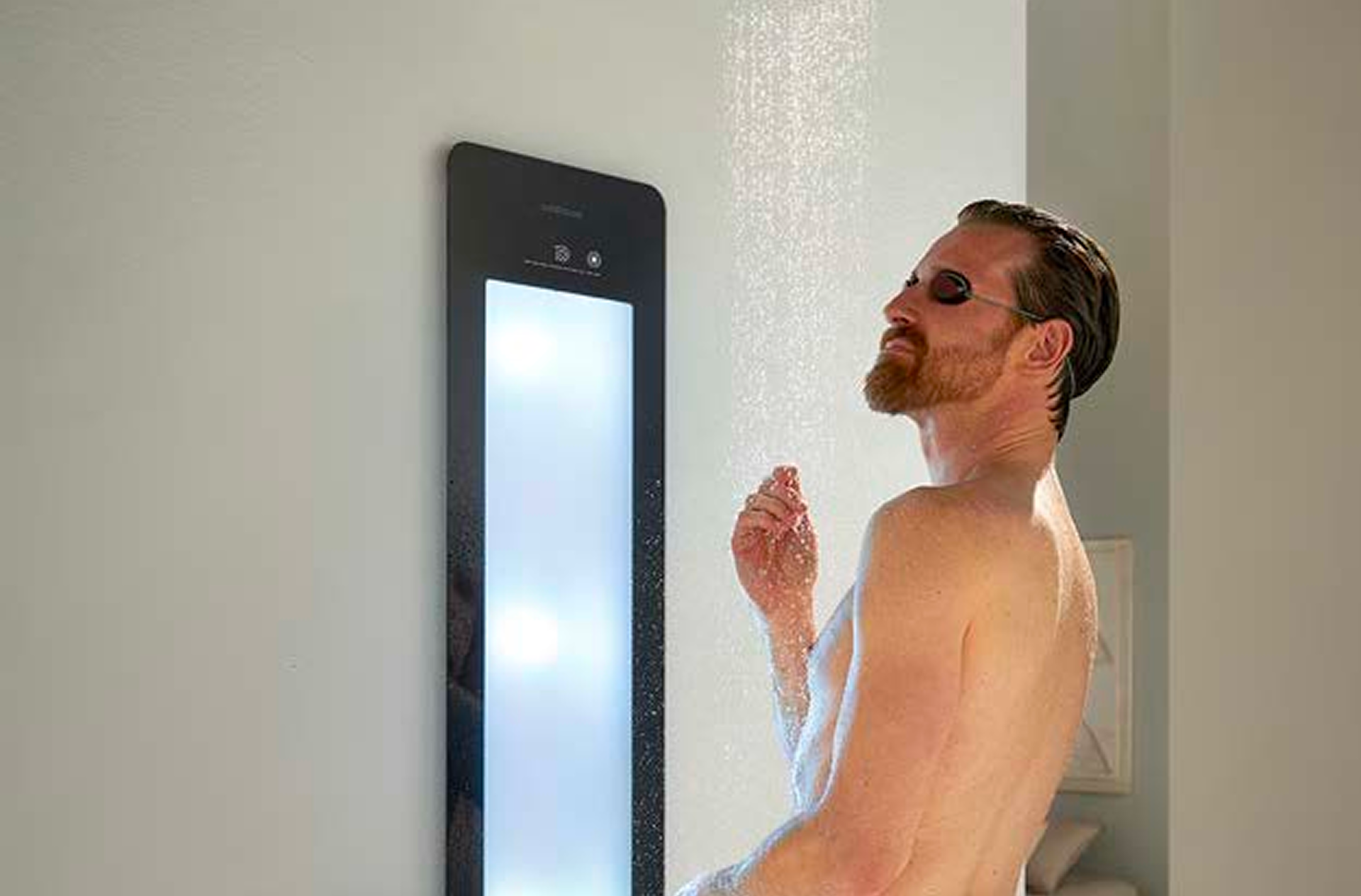 Personne sous la douche avec un panneau Sunshower noir diffusant une lumière blanche éclatante. L’eau tombe en pluie fine. Cette solution pour x²o salles de bains allie sécurité et confort.