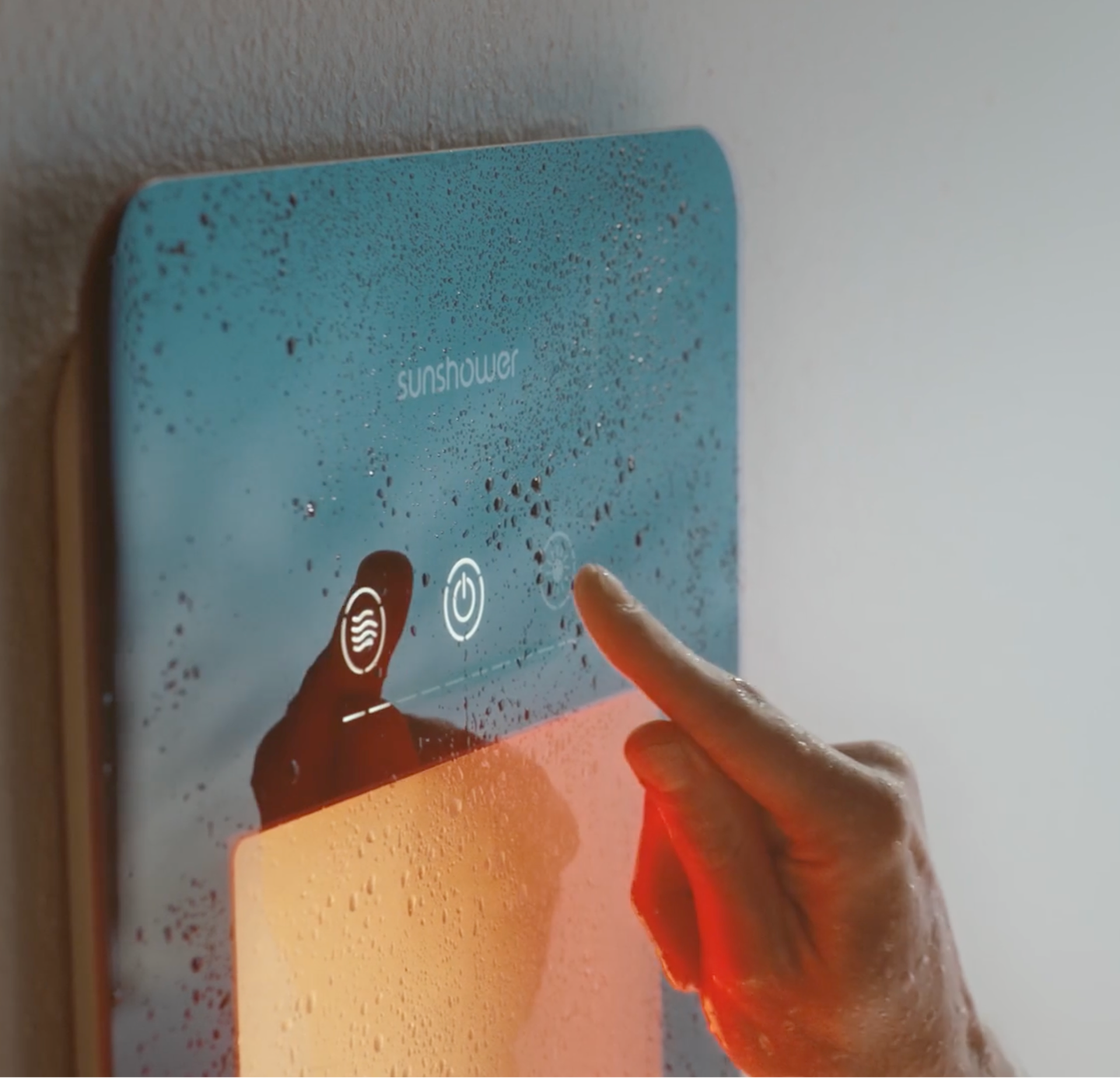 Main qui appuie sur le bouton tactile d’un panneau Sunshower avec surface en verre mouillée et lumière orange intense.
