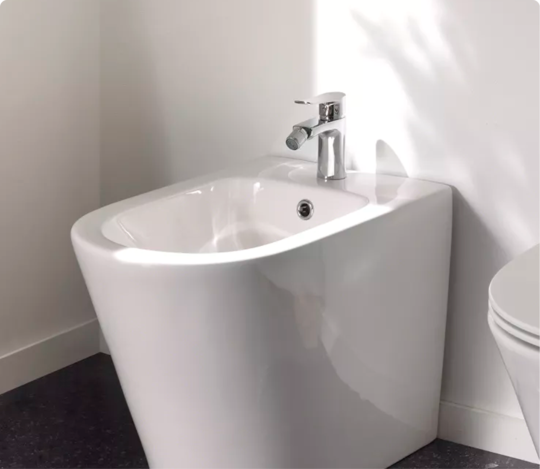  Een wit bidet met chromen kraan, naast een toilet, op een donkere vloer. Functioneel ontwerp van x²o badkamers.