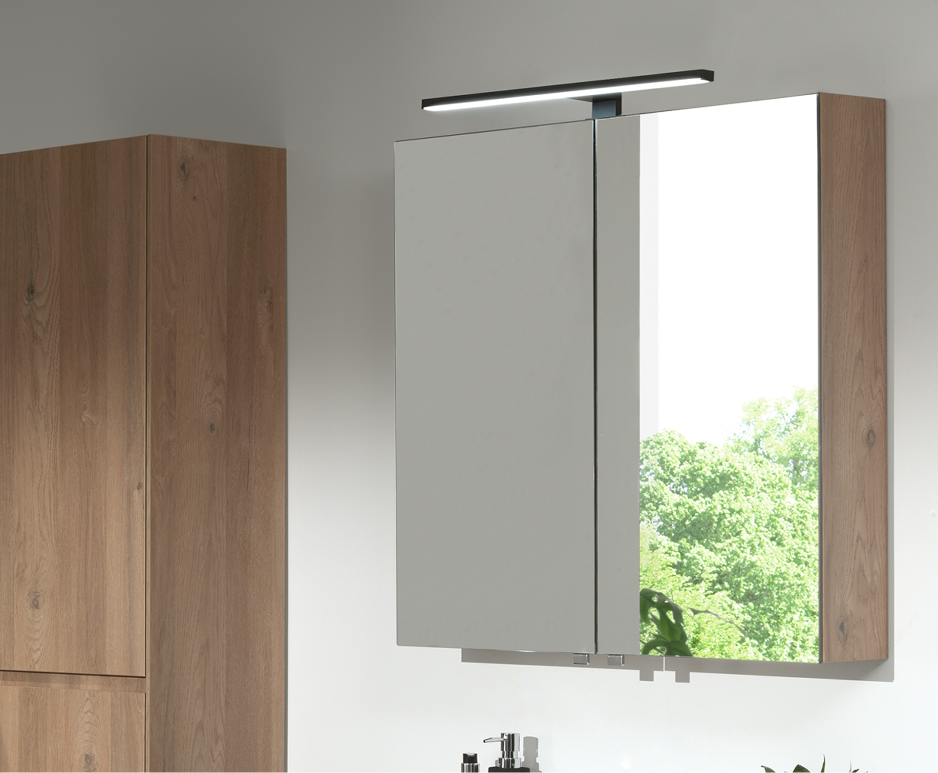 Armoire miroir de x²o salles de bains avec deux portes miroir et côtés en bois, installée au-dessus d’un lavabo avec reflet verdoyant.