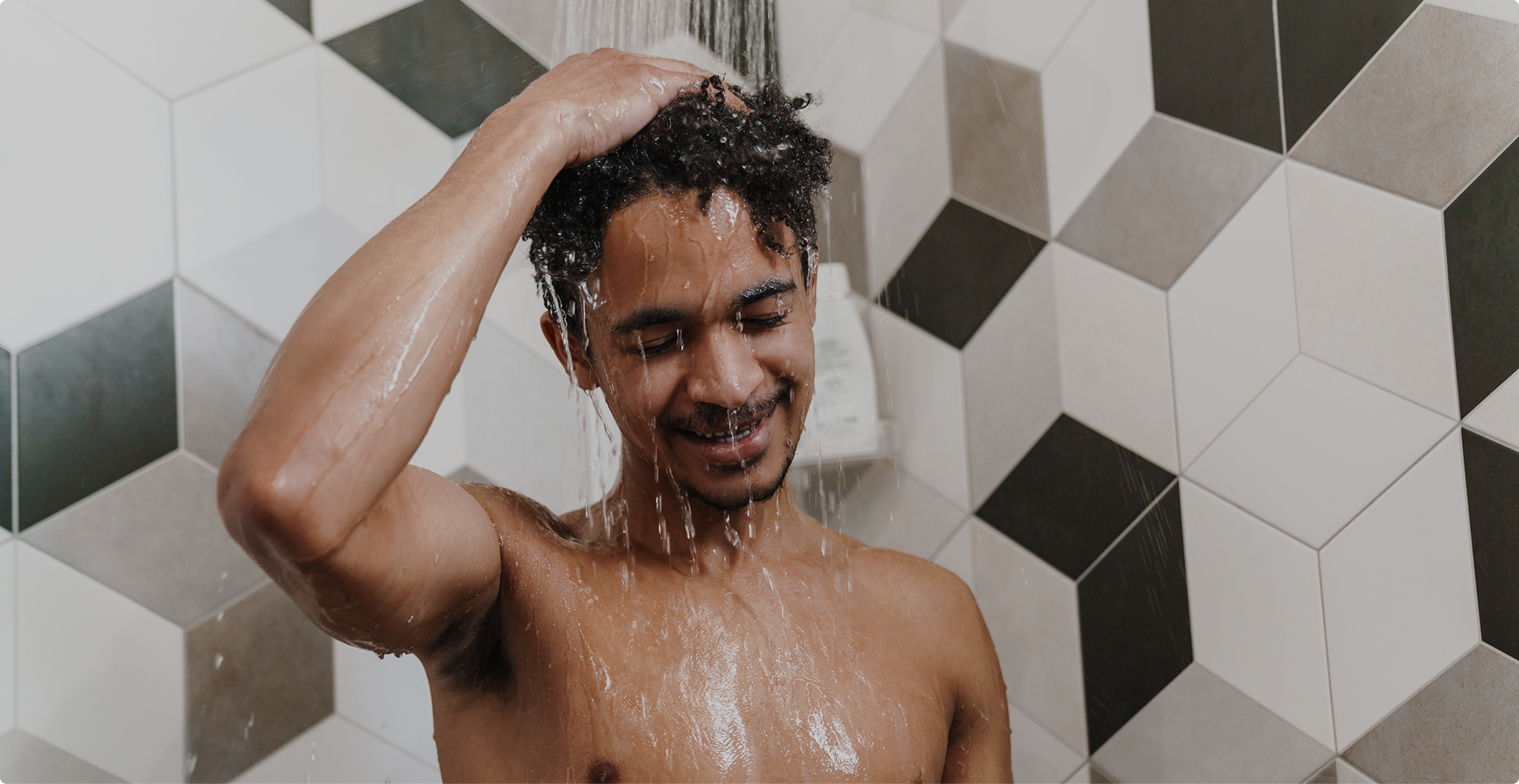 Man geniet van een verfrissende douche in een moderne badkamer met geometrische tegels – X²O Badkamers