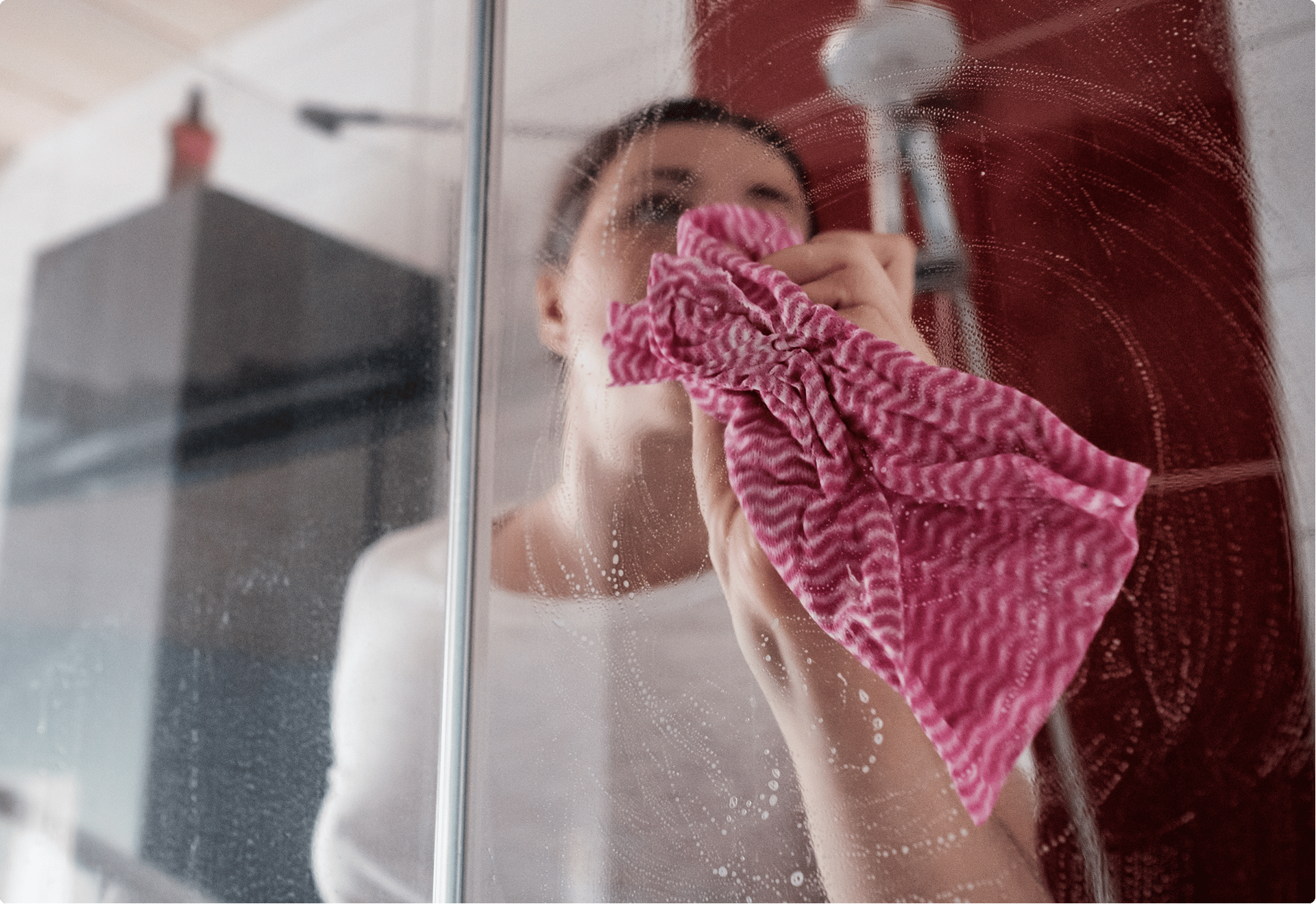 Vrouw maakt de douchewand schoon met een roze doekje – X²O Badkamers