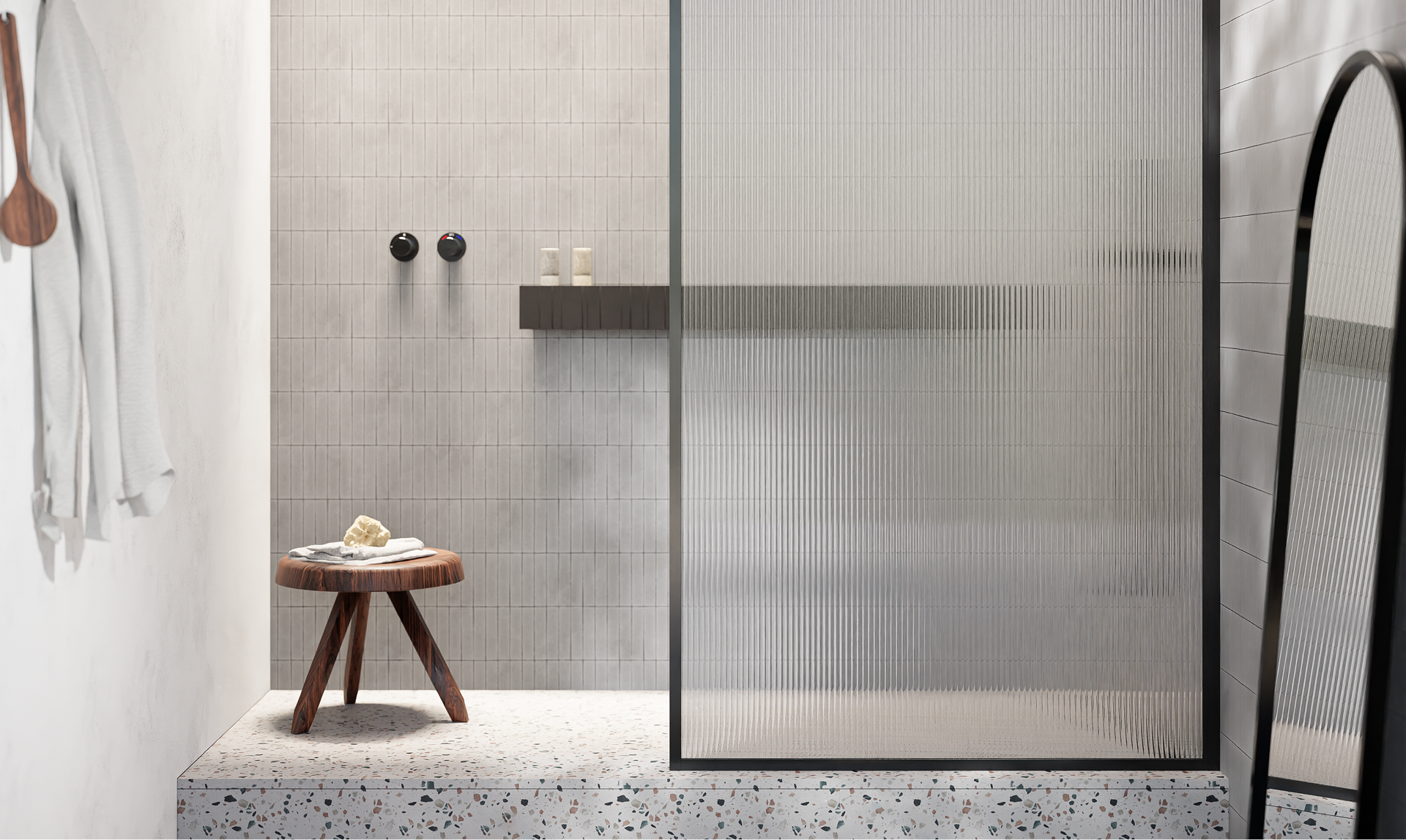 Moderne x²o badkamers inloopdouche met een verhoogd terrazzo-platform, fijne verticale wandtegels in lichtgrijs en een ribbelglas douchewand met zwart kader. Een houten krukje met een handdoek staat links in beeld, en rechts is een grote staande spiegel zichtbaar.