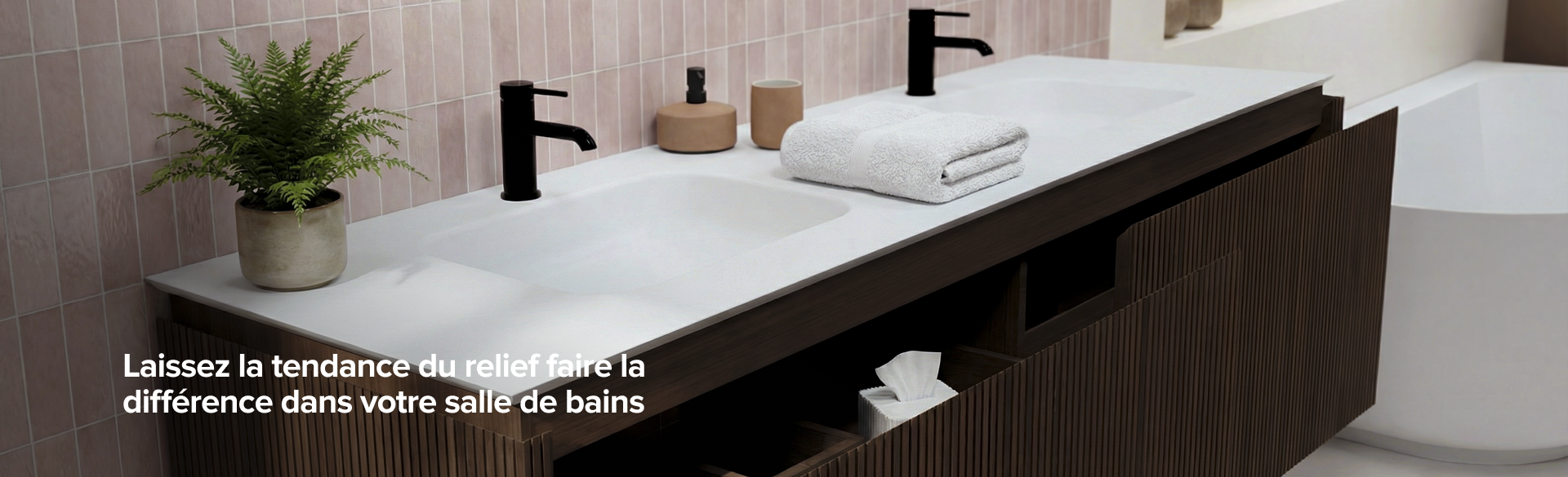 Meuble de salle de bains nervuré brun avec plan vasque blanc, robinets noirs et miroir avec éclairage intégré devant un mur de carreaux rose pastel.