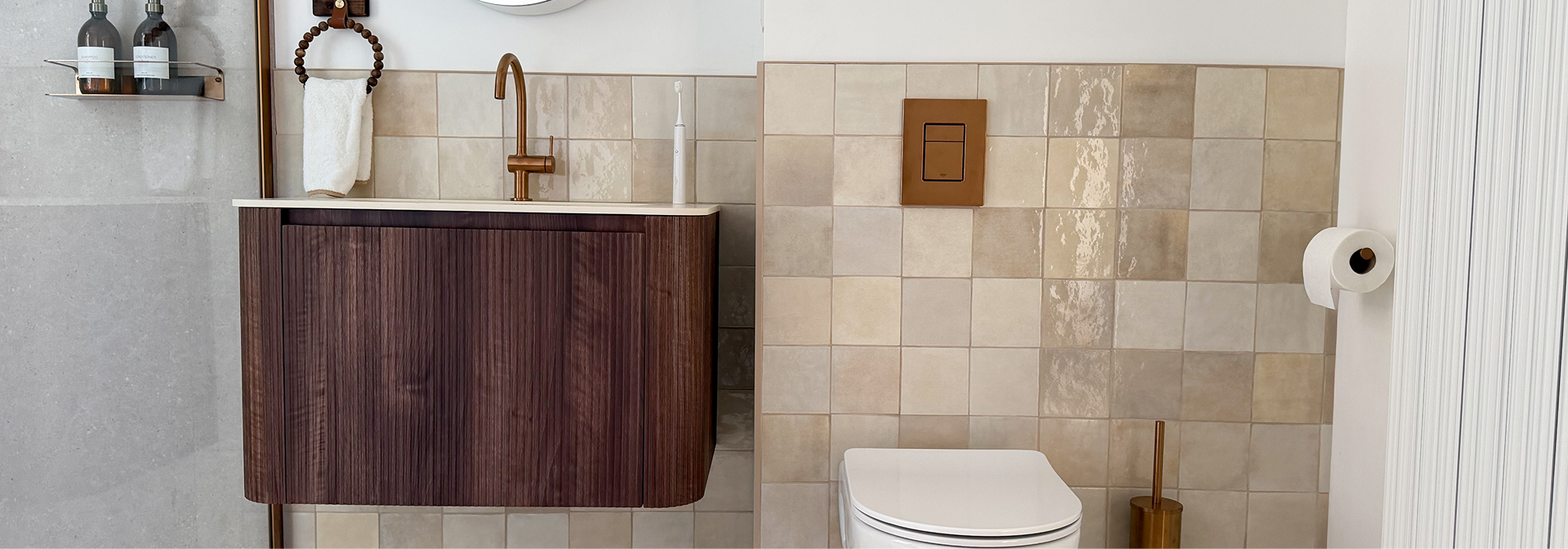 Detail van x²o badkamers meubel in walnootkleur met wastafel, spiegel en accessoires op beige tegelwand.