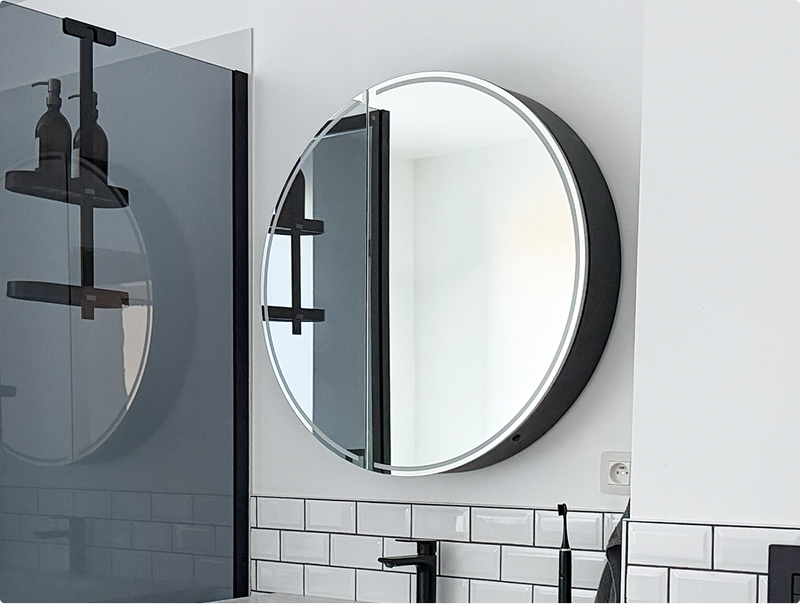 Ronde badkamerspiegel van x²o badkamers met geïntegreerde LED-verlichting boven een wastafel in een moderne zwart-witte ruimte.