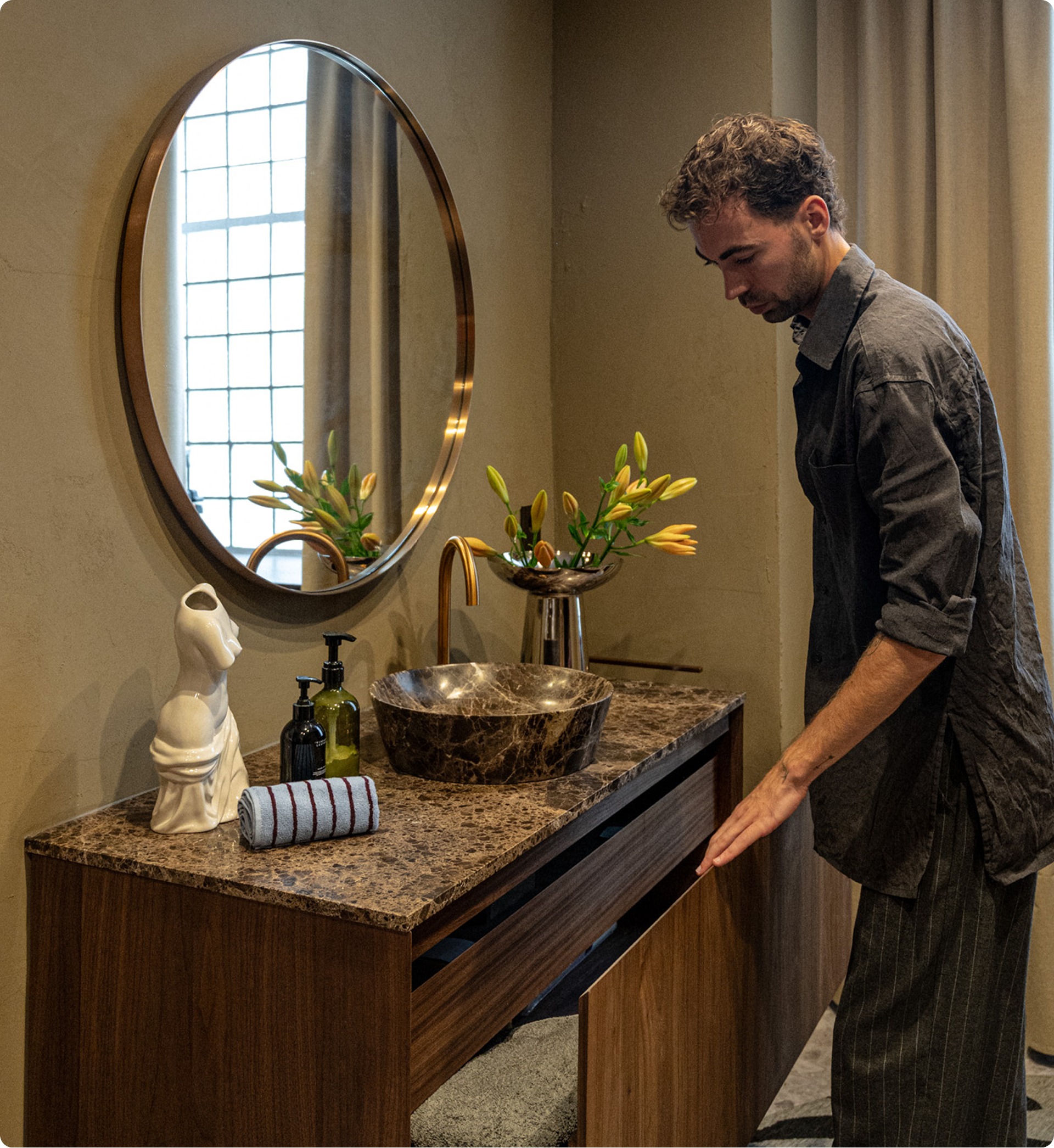 Daan Alferink opent een houten lade van het X²O Badkamers meubel met marmeren blad. Detail van een X²O kraan in geborsteld goud boven een marmeren kom.