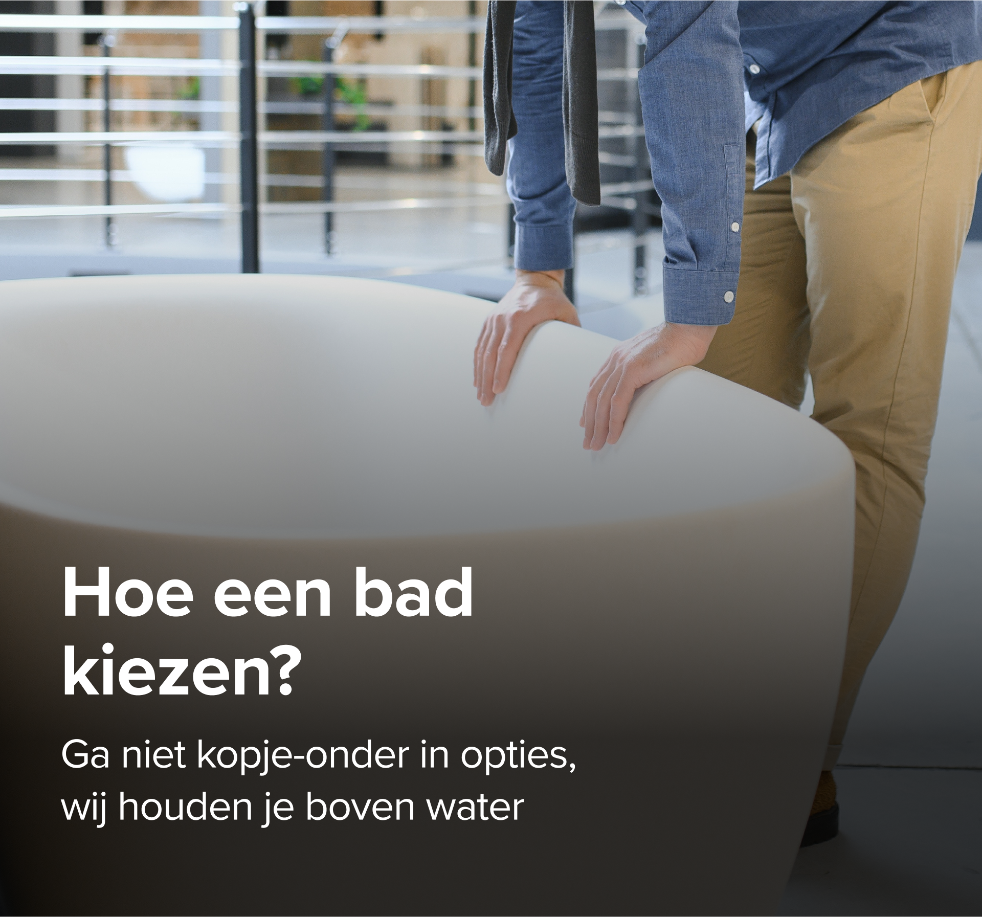 Op deze foto van x²o badkamers zie je een man in beige broek en blauwe blouse die een grote designbadkuip van x²o badkamers bekijkt in een showroom met een industriële vloer en andere badmodellen op de achtergrond.