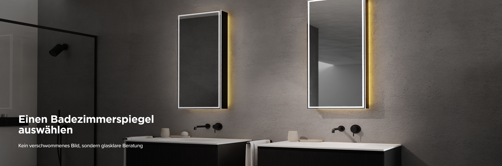 x²o Badezimmer mit zwei beleuchteten vertikalen Spiegeln an grauer Wand, jeweils über einem schwarzen Waschtischunterschrank mit weißem Becken, minimalistischer schwarzer Armatur, beigen Accessoires und einer links sichtbaren schwarzen Walk-in-Dusche.
