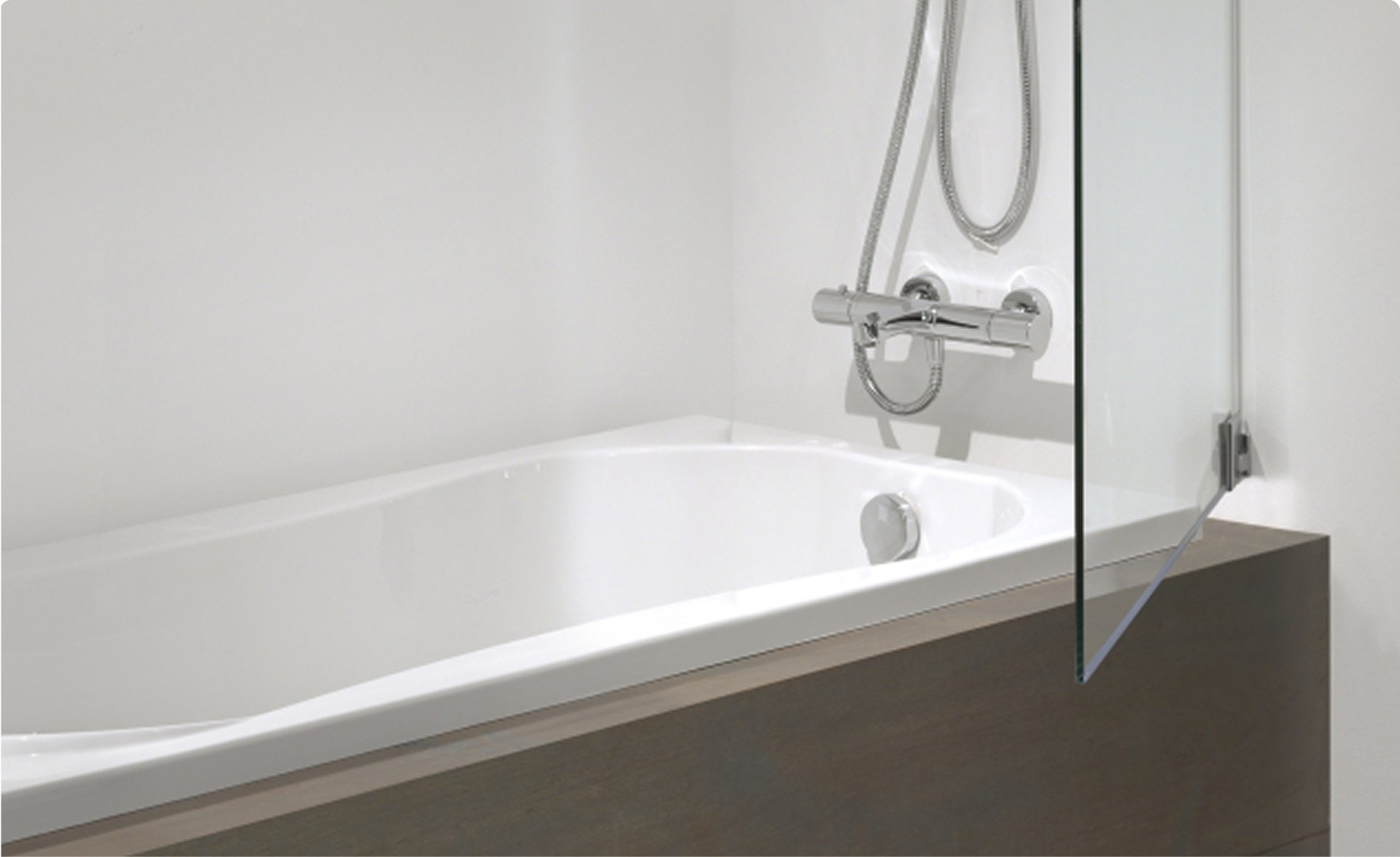 Ingebouwd wit ligbad met glazen badwand en chromen thermostatische kraan met handdouche, geplaatst tegen een witte wand met houten badombouw, in een badkamer van x²o badkamers.