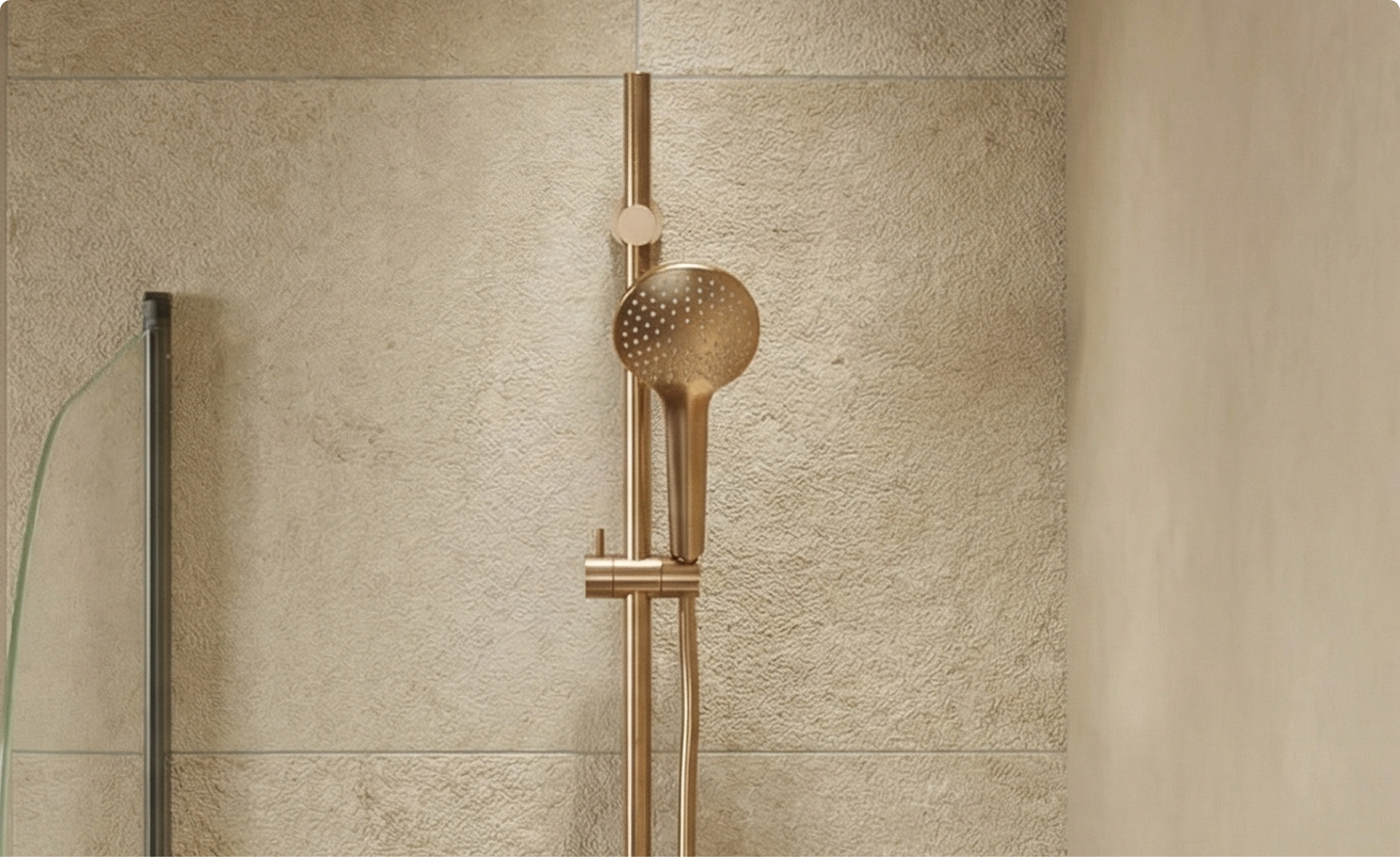 Goudkleurige handdouche met ronde sproeikop gemonteerd op een verticale glijstang tegen een licht gestructureerde wand, in een badkamer van x²o badkamers.