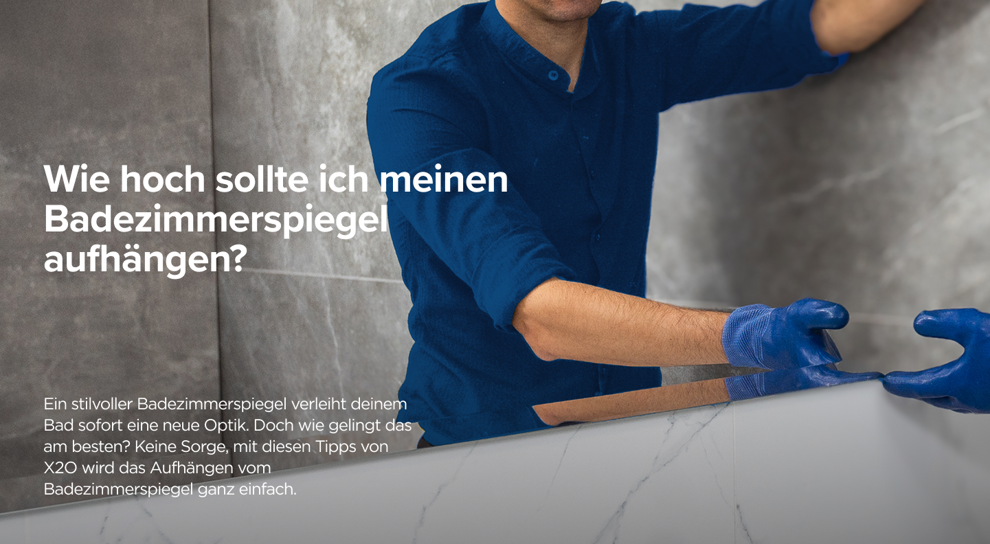 Ein Handwerker in blauer Arbeitskleidung befestigt einen Spiegel an einer Marmor-Optik-Wand im Bad – praktische Anleitung von x²o badkamers.