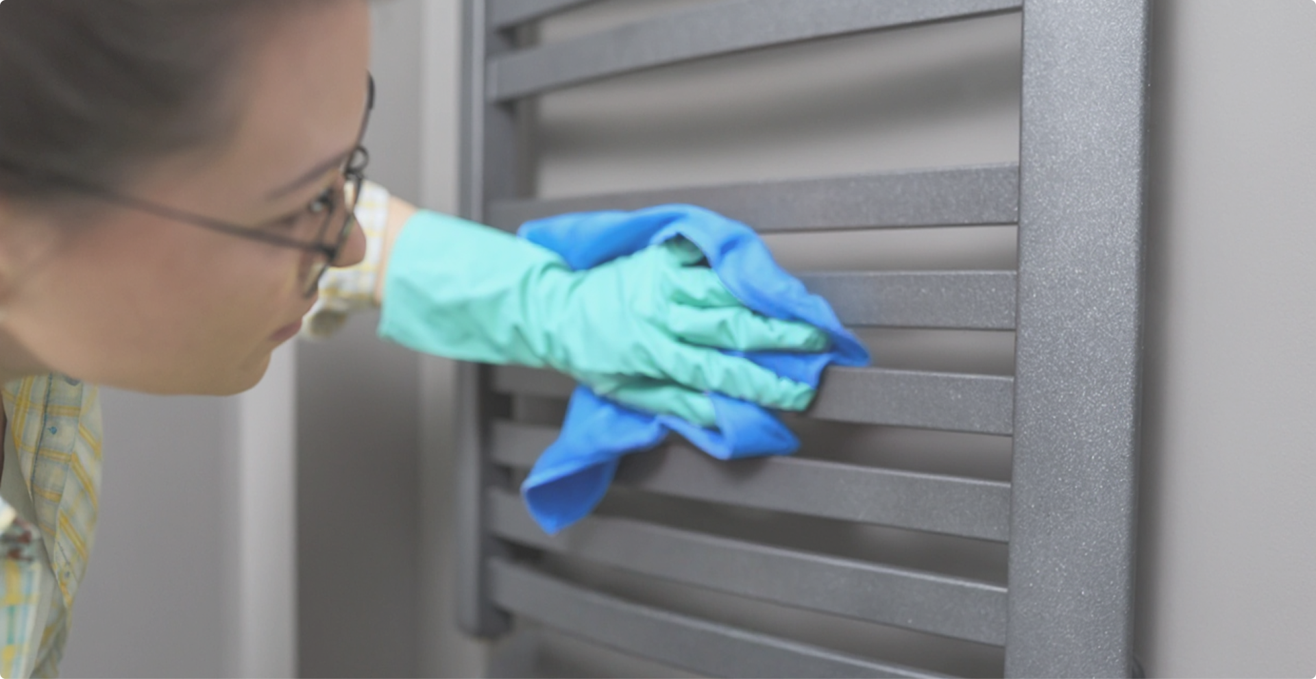 “Femme nettoie soigneusement un radiateur gris avec gants dans un intérieur X2O salles de bains.”
