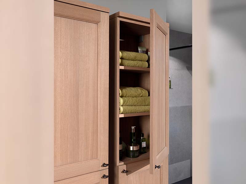 Open houten badkamerkast met planken gevuld met groene handdoeken en verzorgingsproducten.