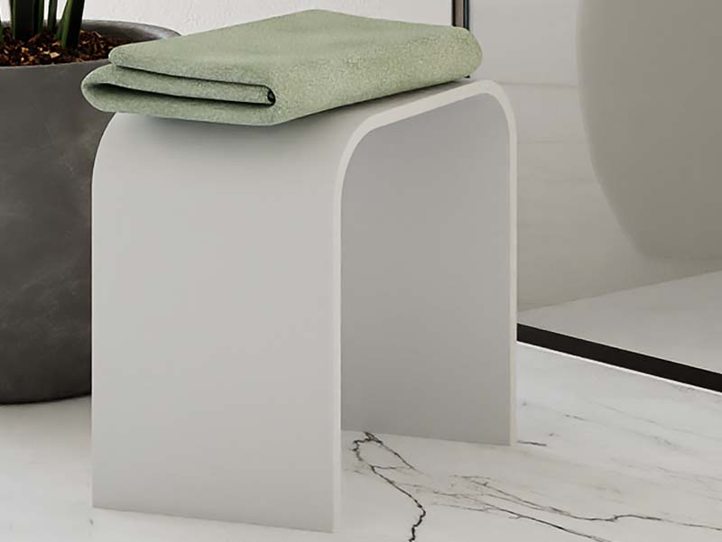Moderner weißer Badezimmerhocker mit abgerundeten Kanten, darauf ein gefaltetes grünes Handtuch.