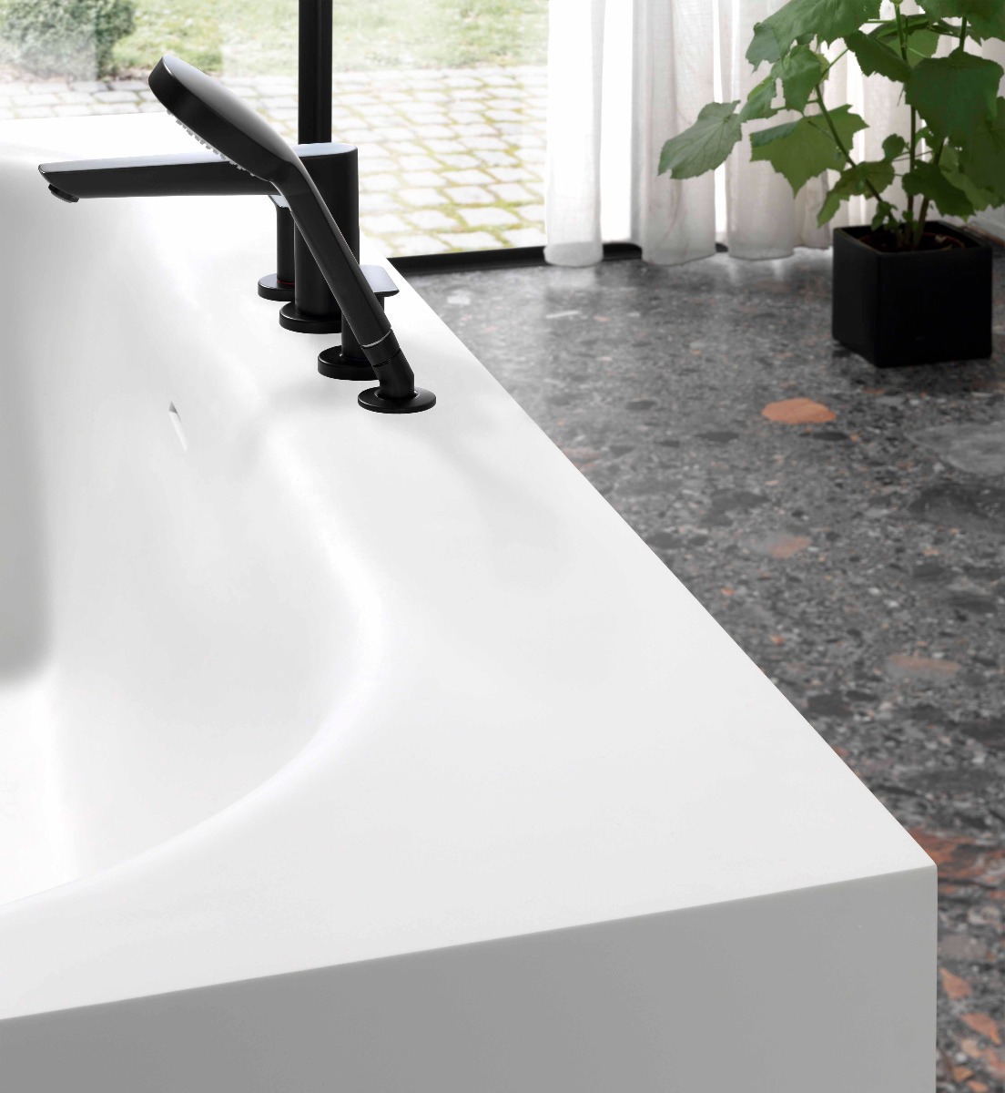 Nahaufnahme einer weißen Badewanne mit mattschwarzem Wasserhahn und Handbrause auf Marmorboden.