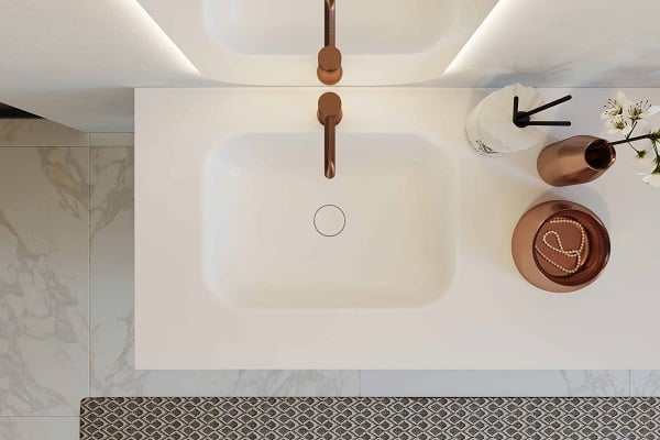 Moderne weiße Waschbeckenplatte mit integriertem Becken und kupferfarbenem Wasserhahn auf Marmorboden.