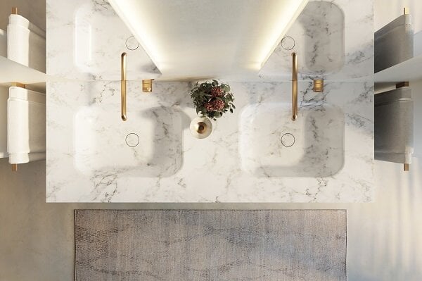 Zwei Marmorwaschbecken mit goldenen Wasserhähnen und einem Blumenarrangement in der Mitte, von oben betrachtet.