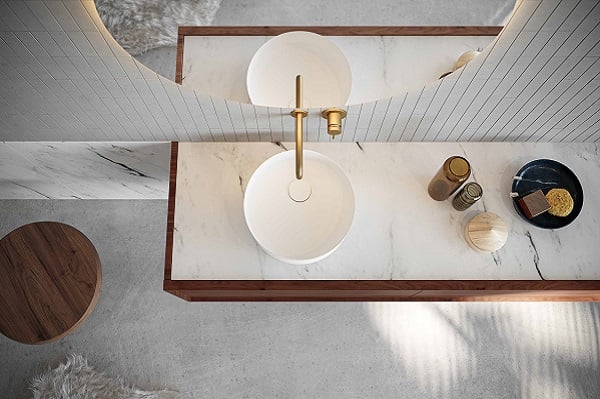 Weiße Waschbecken mit goldenen Wasserhähnen auf einer Marmorplatte mit einem Holzgestell, von oben betrachtet.