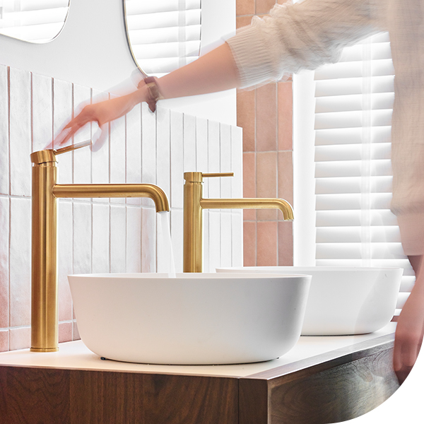 Dubbele witte wastafels met gouden kranen en een moderne badkamerwand met witte tegels.