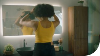 Femme se brosse les cheveux devant le miroir dans la salle de bains avec lavabo moderne