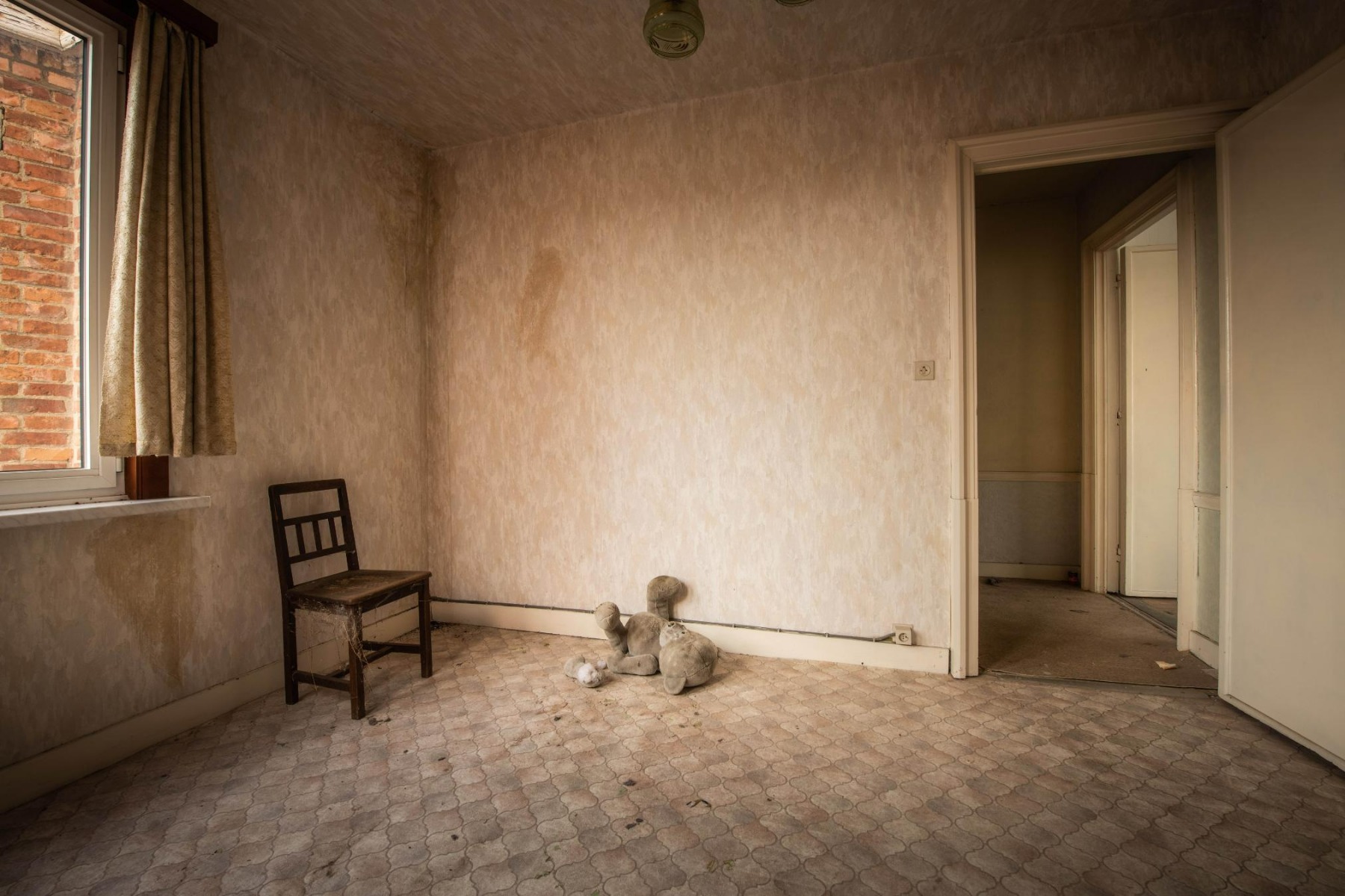 Vernachlässigtes Zimmer mit einem Holzstuhl, einem Teddybär auf dem Boden und verblassten Wänden