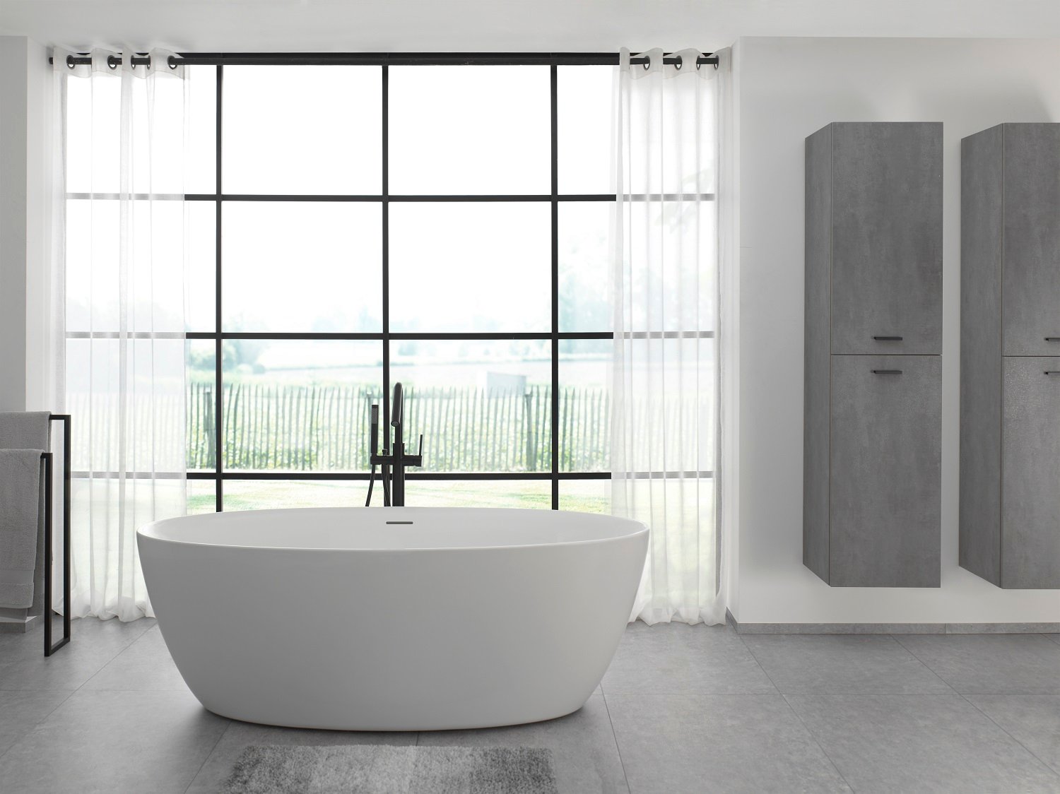 Freistehende Badewanne Luca Varess Dias aus mattem Acryl von x²o Badezimmer, platziert vor einem großen Fenster mit Blick ins Grüne. Die weichen Formen und die schwarze Standarmatur verleihen dem Raum eine ruhige und moderne Atmosphäre.